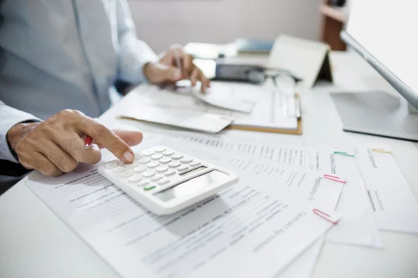A professional calculating figures with a calculator while reviewing tax forms and business documents on a desk.