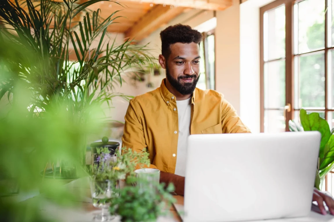 A man in an orange shirt sitting in his home office on a video call.