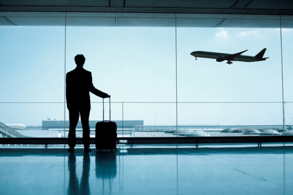 Silhouette of a business traveller with luggage looking out an airport terminal window at an airplane landing. 